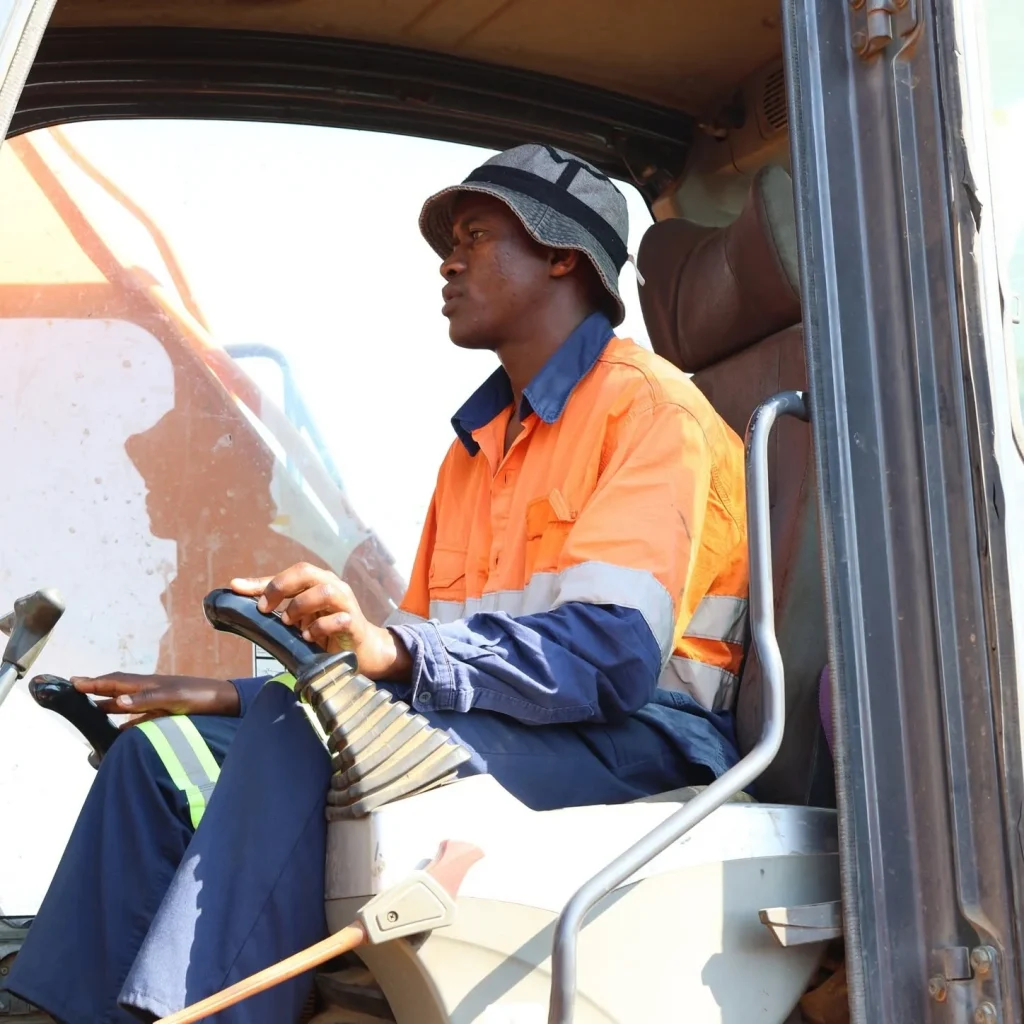 Learner in hi-visibility clothing seated at the controls of an excavator with both hands on the joysticks.